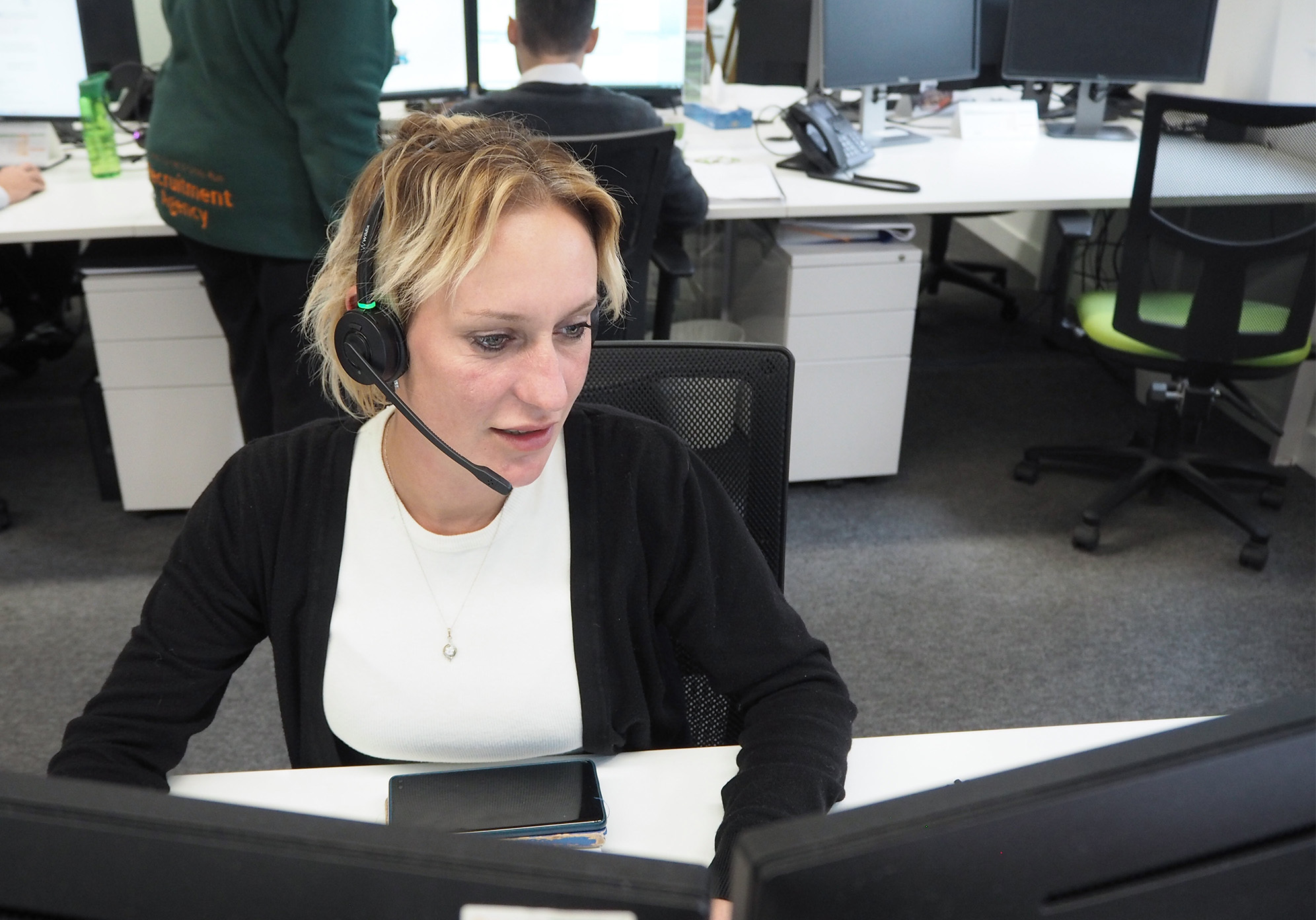Nikita is wearing a headset whilst speaking to a client and looking at two computer monitors in front of her.