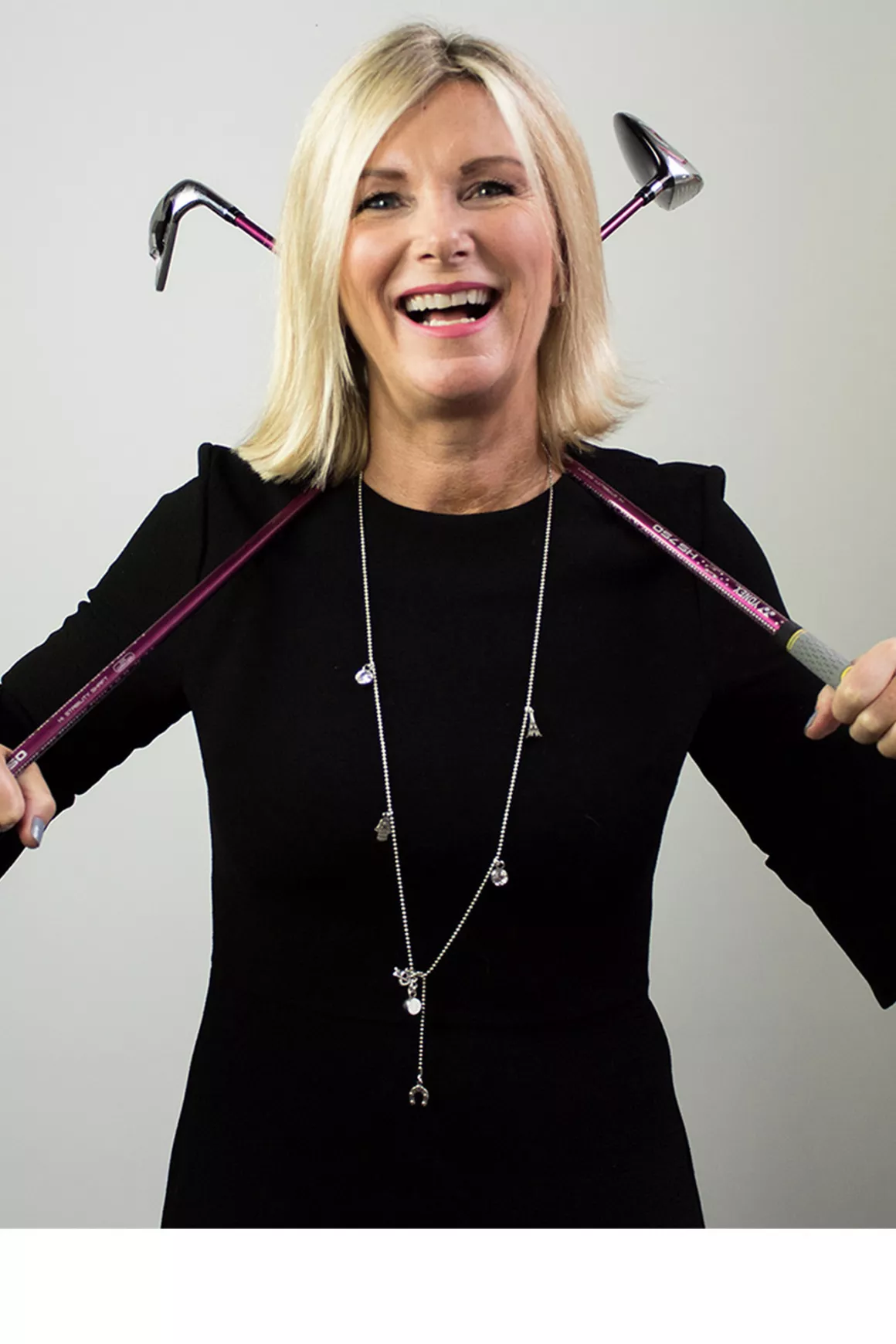 Robyn Holmes (MD) of Prime Appointments, wearing black dress holding golf clubs in both hands, photo taken with a white background